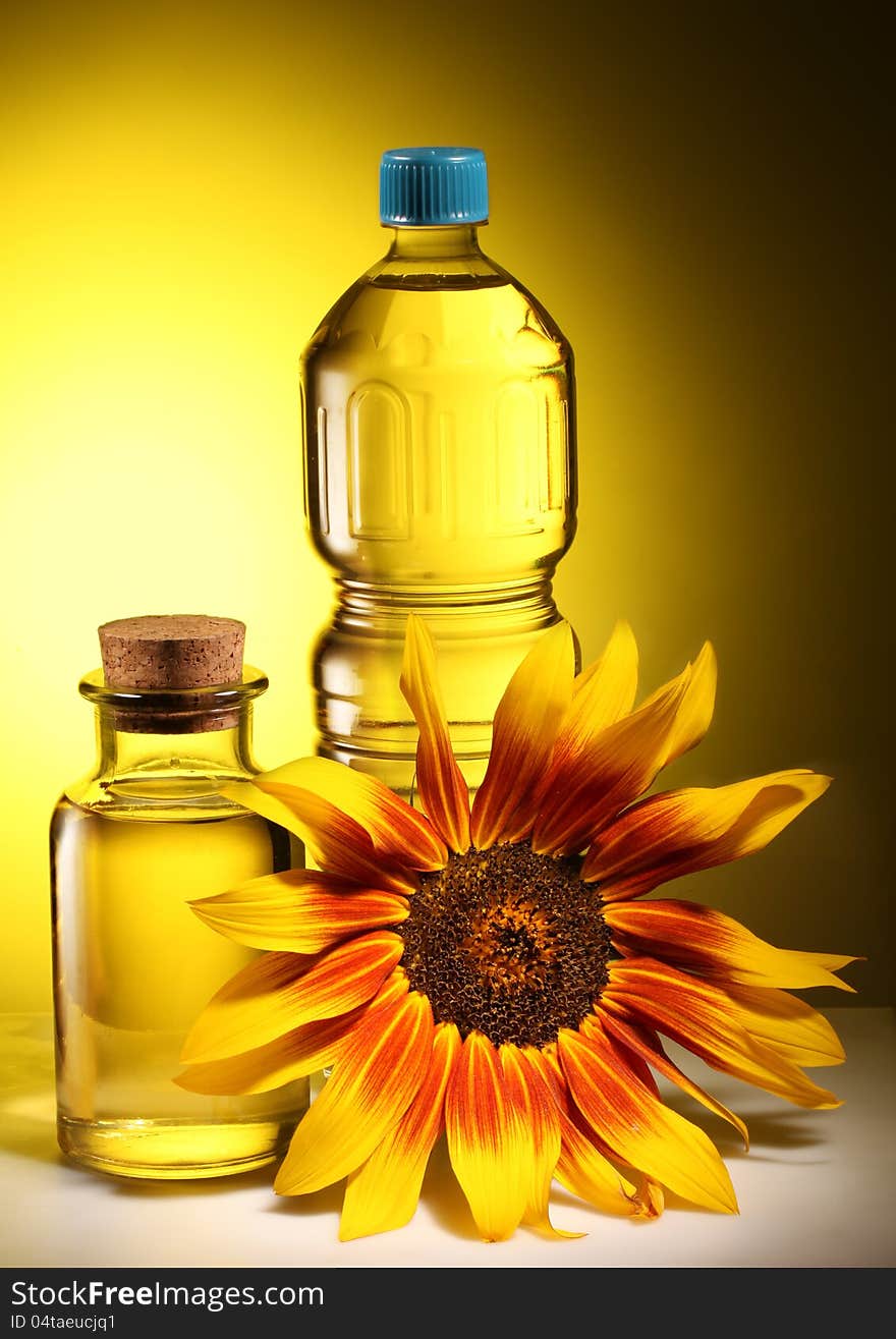 Cooking oil in a plastic and glass bottles with sunflower on a dark yellow background. Cooking oil in a plastic and glass bottles with sunflower on a dark yellow background.