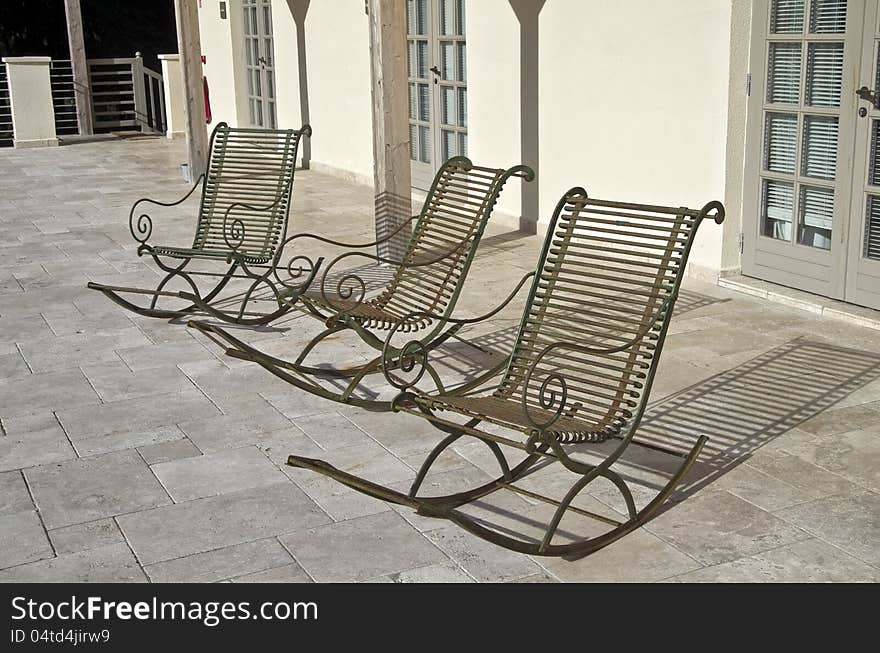 Three empty metal rocking chairs in front of the house. Three empty metal rocking chairs in front of the house.