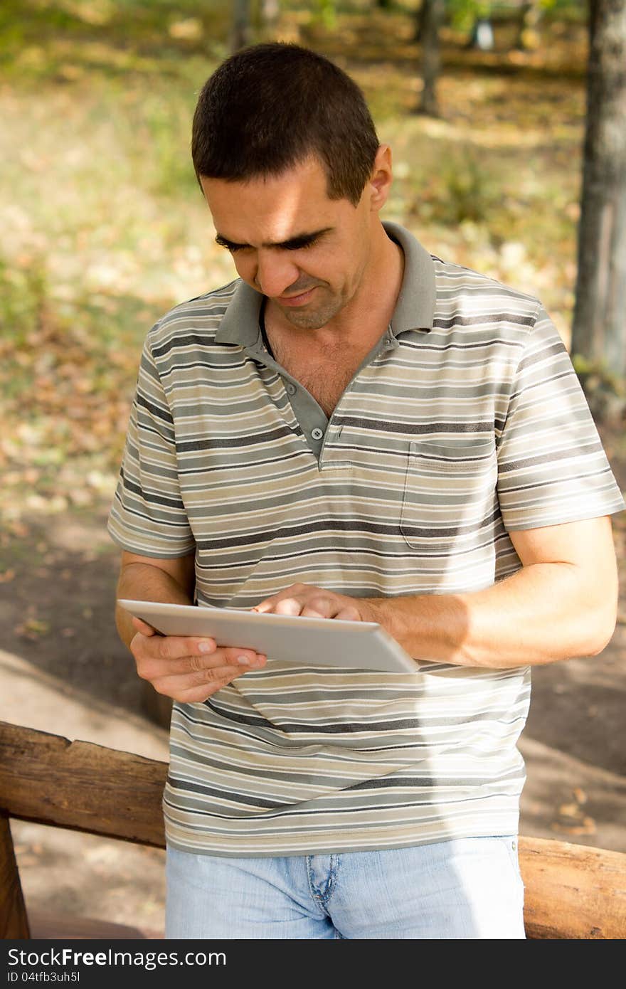 Casual middle-aged man standing typing on a touchscreen tablet that he is holding in his hand. Casual middle-aged man standing typing on a touchscreen tablet that he is holding in his hand