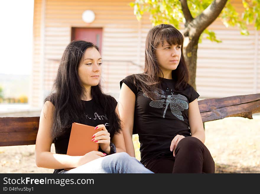 Two sad or thoughtful looking women sittng on a bench outdoors with a book. Two sad or thoughtful looking women sittng on a bench outdoors with a book.