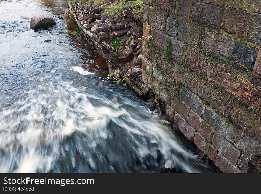 Turbulent river flows along the ruined stone wall