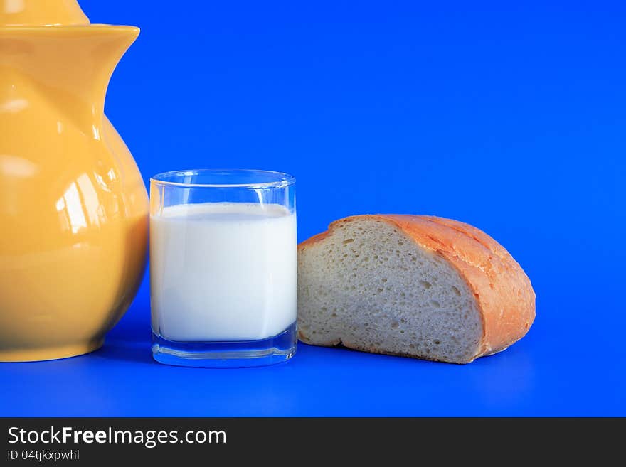 Glass full of milk and bread near yellow pitcher on blue background