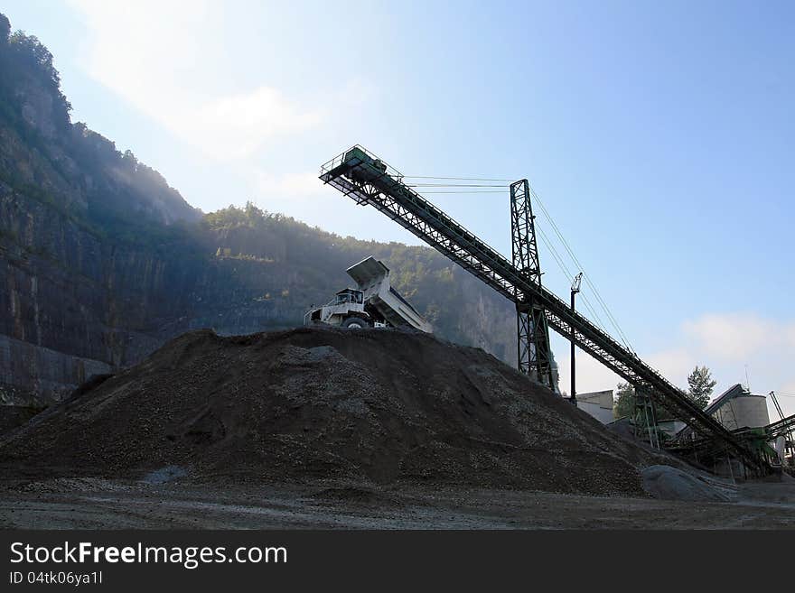 A conveyor belt and a truck in a gravel pit with morning fog