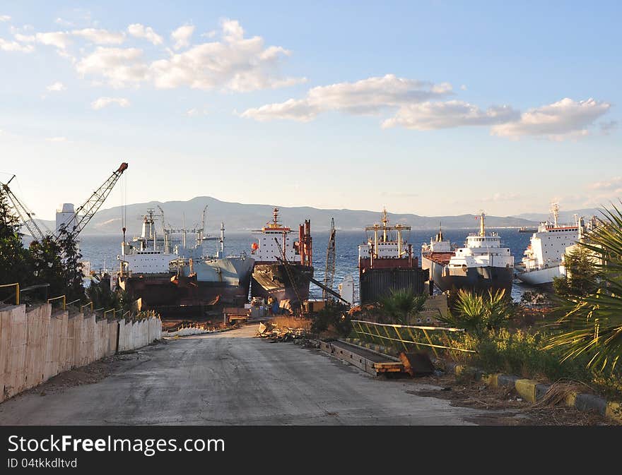 Scrapyard with cranes where large ships docked at the coast waiting for dismantling under blue sky with clouds. Aliaağa, Turkey. Scrapyard with cranes where large ships docked at the coast waiting for dismantling under blue sky with clouds. Aliaağa, Turkey.