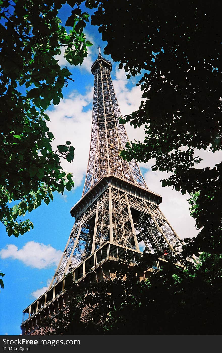 Photo of the Eiffel Tower with branches full of leaves and sky with clouds. Photo of the Eiffel Tower with branches full of leaves and sky with clouds