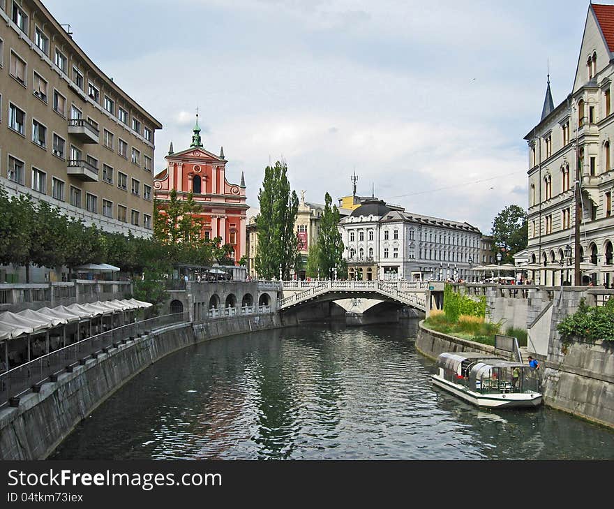 The waterfront in the historic center of Ljubljana, we see the triple deck and a view of the square and the Franciscan Church of the Annunciation Preseren with its distinctive red and pink façade. The waterfront in the historic center of Ljubljana, we see the triple deck and a view of the square and the Franciscan Church of the Annunciation Preseren with its distinctive red and pink façade