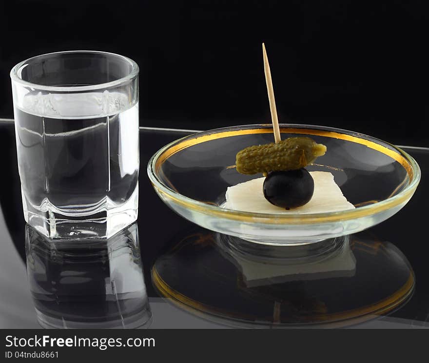 Glass of vodka and dish with snack on black reflective background. Glass of vodka and dish with snack on black reflective background