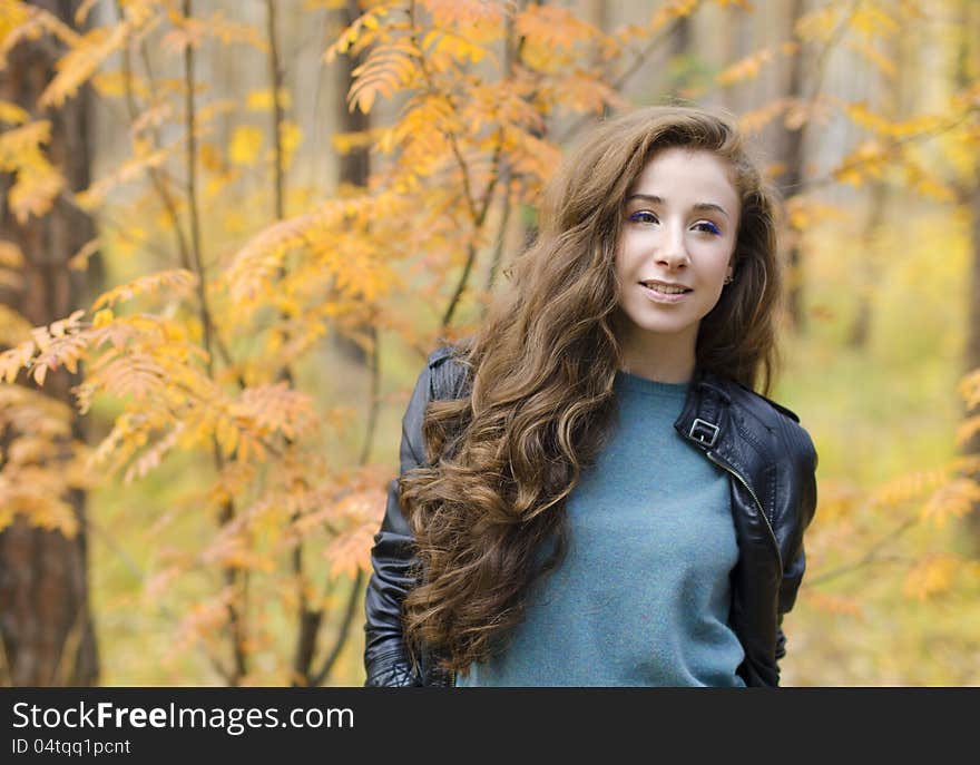 Portrait of smiling girl sitting near the tree in autumn forest