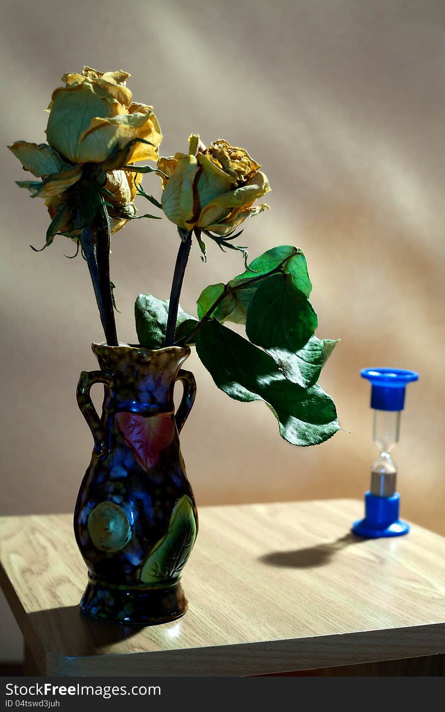 Vase with yellow dried roses and hourglass