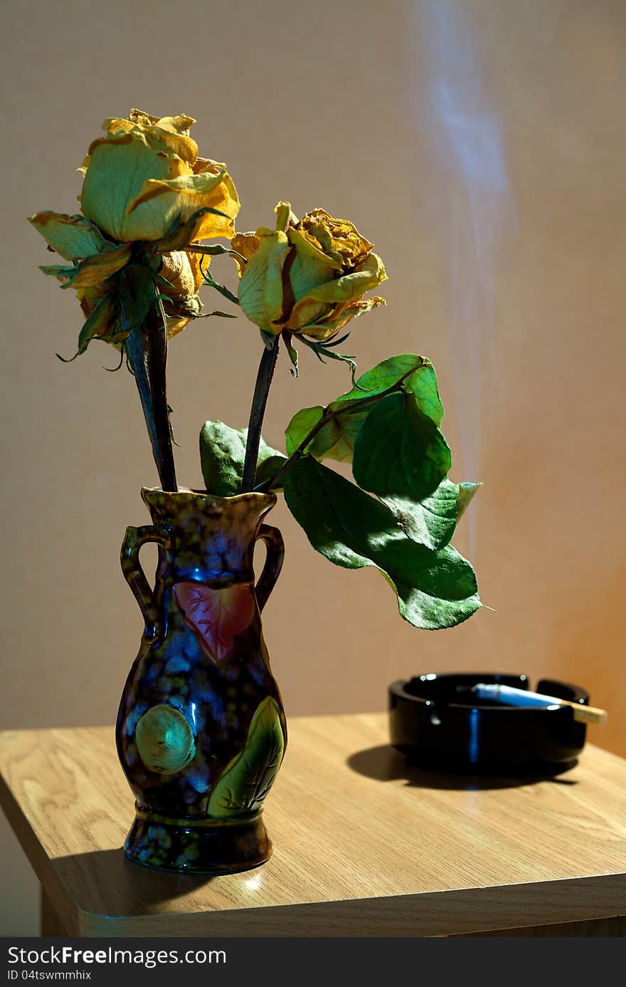 Vase with yellow dried roses and ashtray