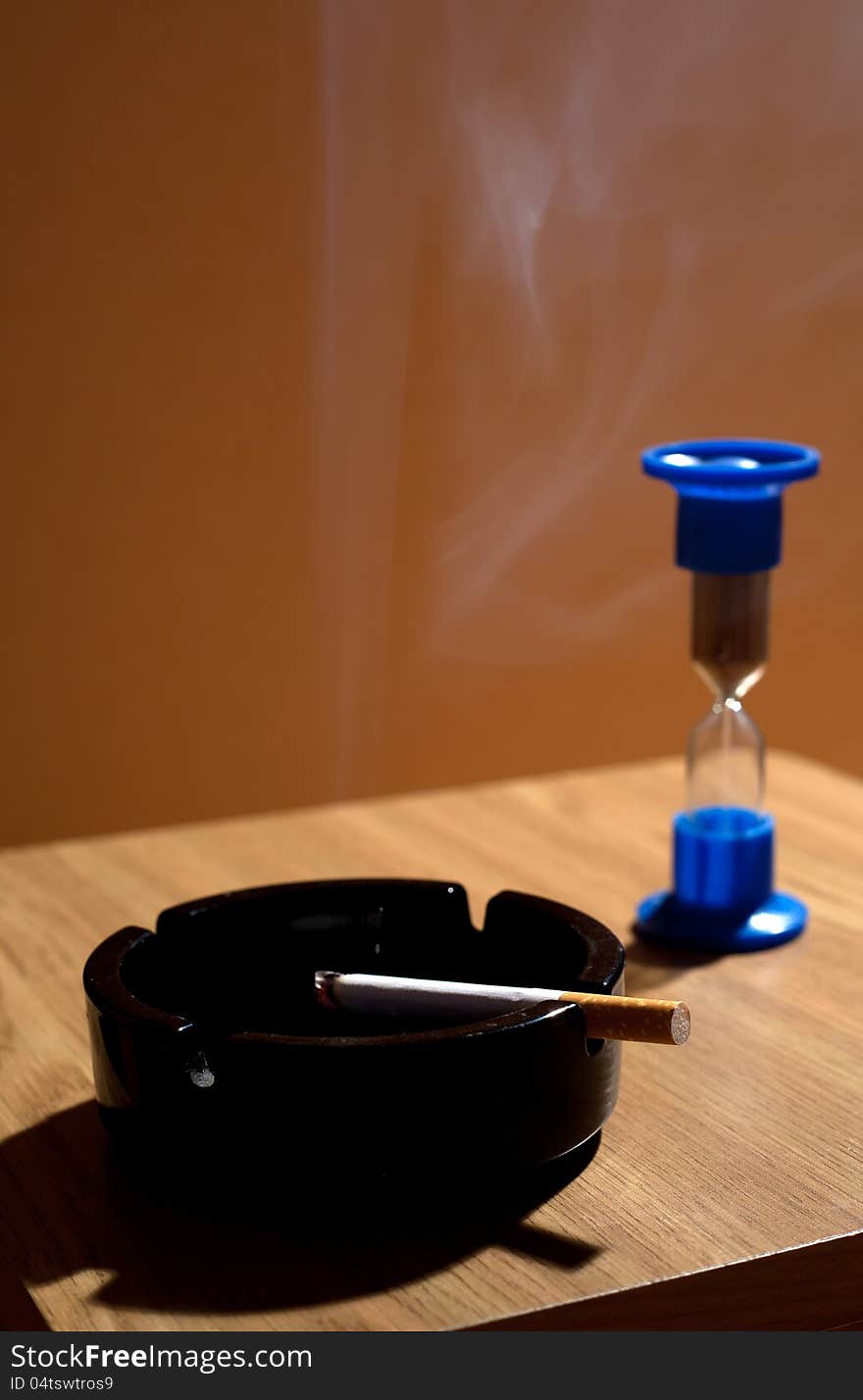 Ashtray with cigarette and hourglass closeup in studio