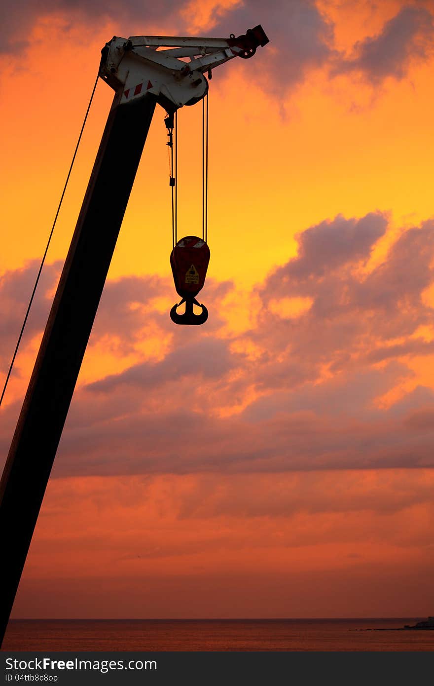 Silhouettes of a boom truck with a hook at dawn