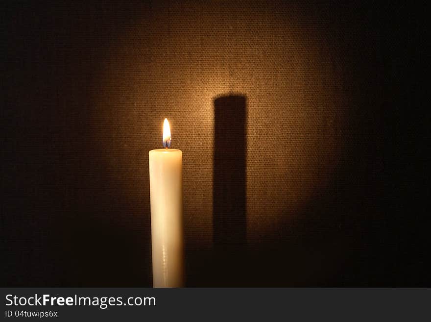 Lighting candle with long shadow against canvas background. Lighting candle with long shadow against canvas background