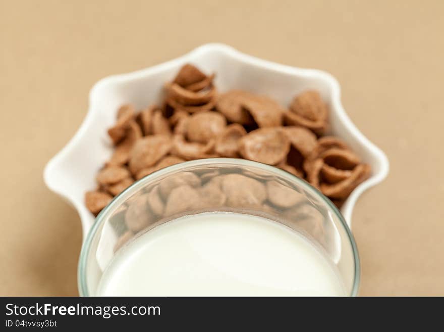 Chocolate cornflakes in white bowl and milk  glass in sepia background. Chocolate cornflakes in white bowl and milk  glass in sepia background