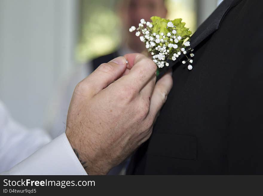 The grooms father places the boutonniere on the groom in preparation of their wedding. The grooms father places the boutonniere on the groom in preparation of their wedding