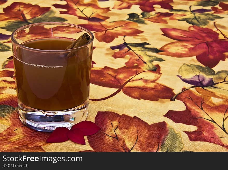 Glass of apple cider with cinnamon stick on autumn table