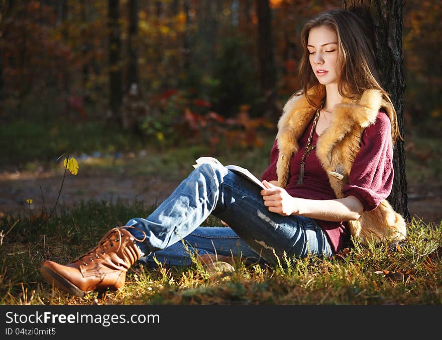 Beautiful autumn girl reading a book in the forest