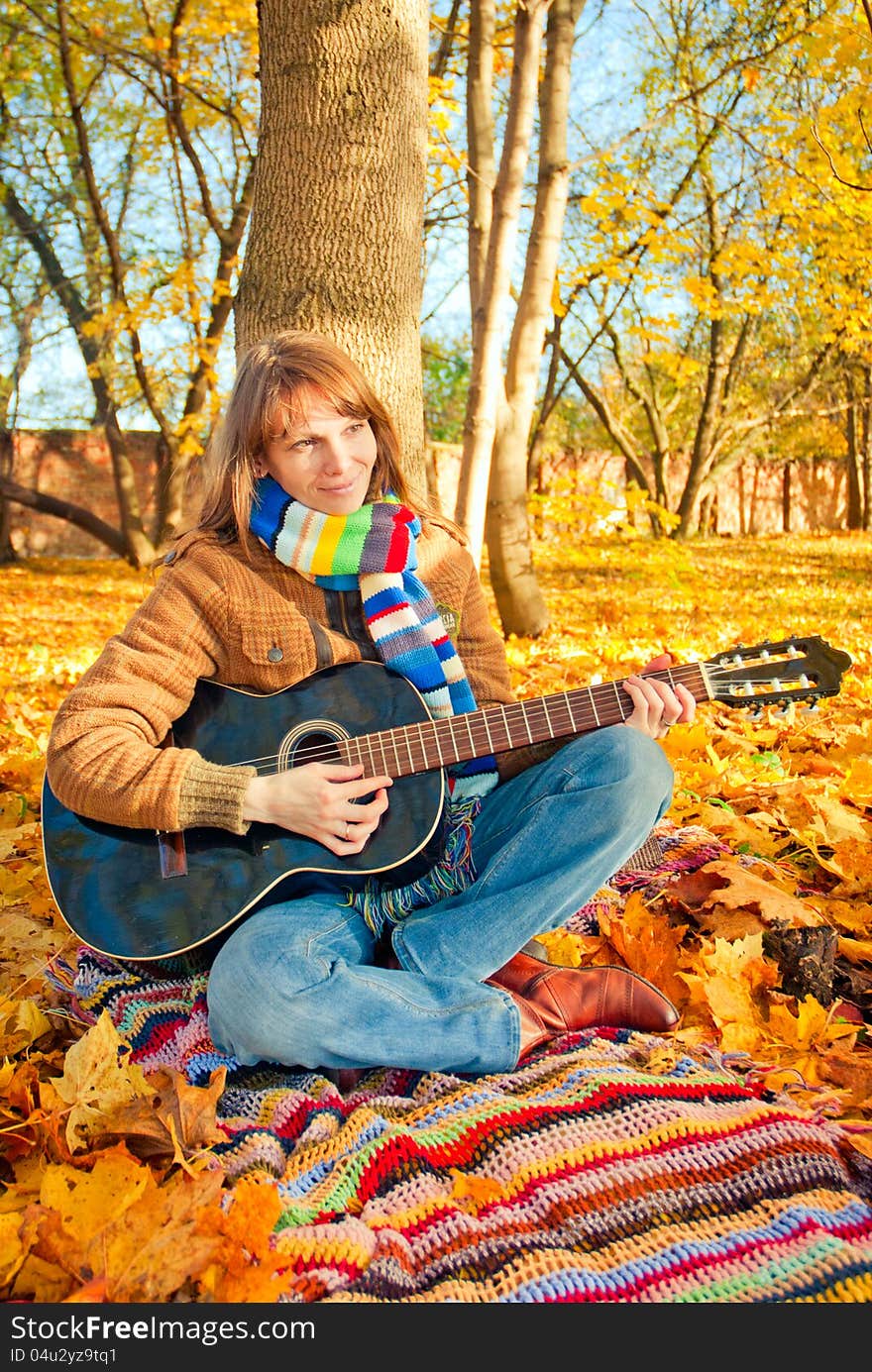 Young romantic girl sitting in autumn park with guitar