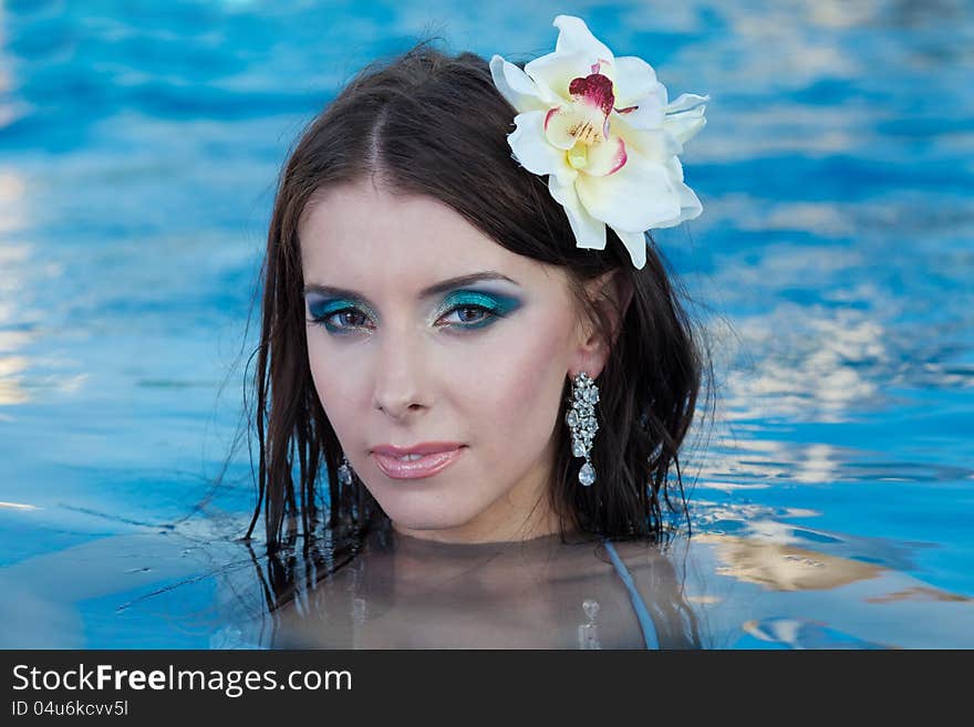 Portrait of the beautiful girl with a flower in hair against blue water. Portrait of the beautiful girl with a flower in hair against blue water