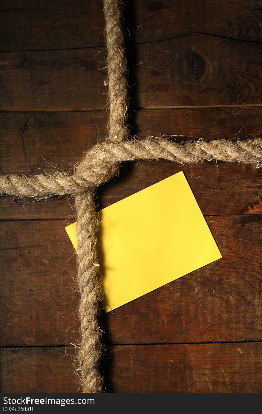 Blank yellow paper attached to wooden surface with rope. Blank yellow paper attached to wooden surface with rope