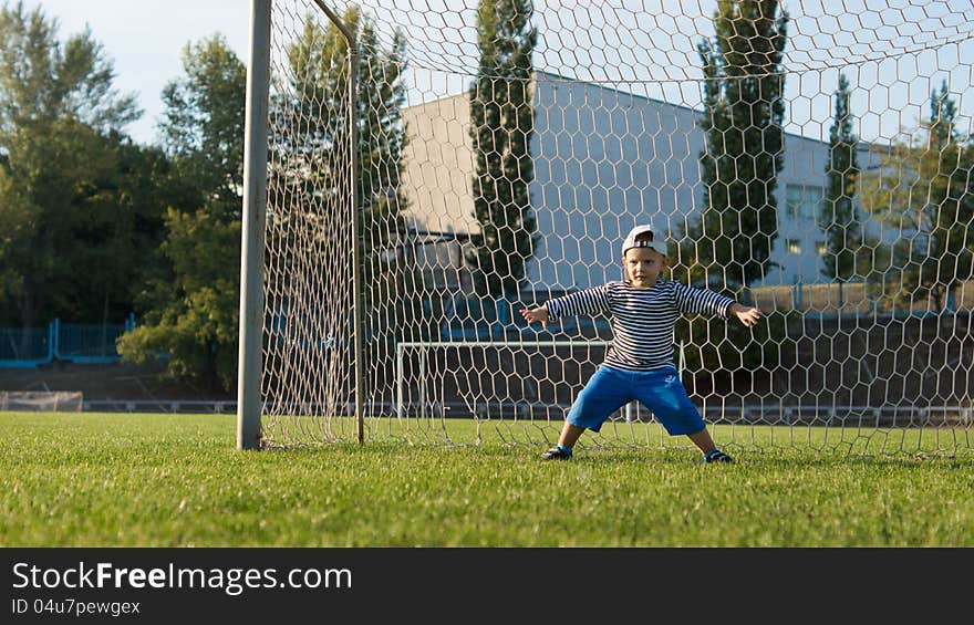 Young little goalie wearing a backwards cap standing in the goals with his legs and arms spread wide protecting the goal line