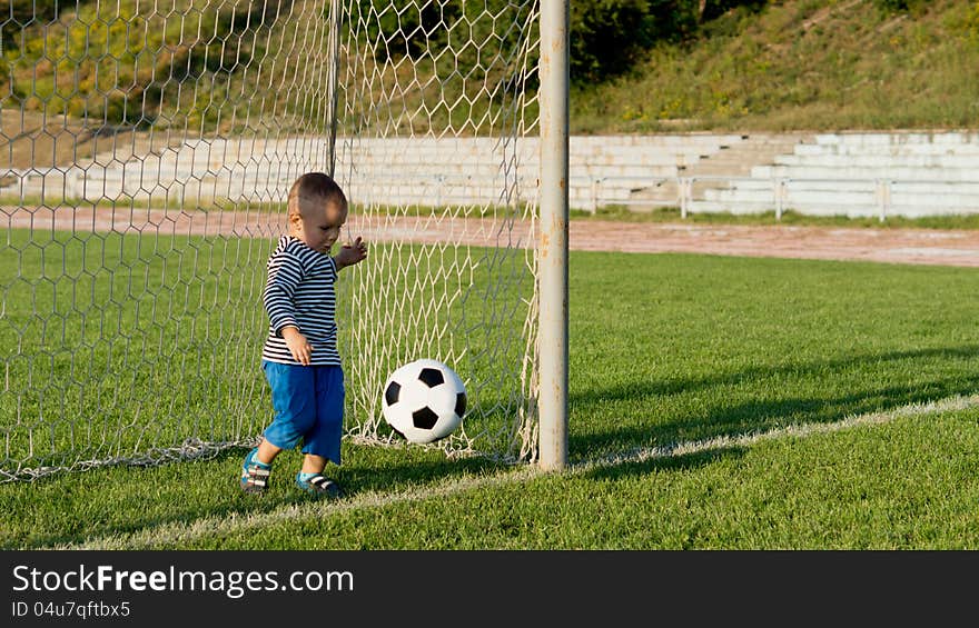 Little boy playing at being a goalkeeper kicking a soccer ball away from the goal line on a green playing field. Little boy playing at being a goalkeeper kicking a soccer ball away from the goal line on a green playing field