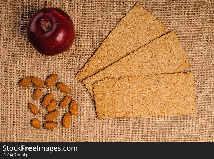 Red apple with crispbread and almonds on sacking background