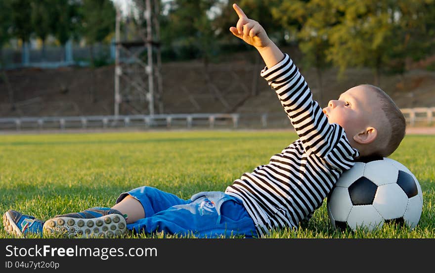 Little boy lying on his back in green grass with his head resting on a soccer ball pointing at the sky. Little boy lying on his back in green grass with his head resting on a soccer ball pointing at the sky