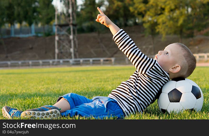 Small boy lying on his back on a grassy playing field with his head resting on a soccer ball pointing at the sky. Small boy lying on his back on a grassy playing field with his head resting on a soccer ball pointing at the sky