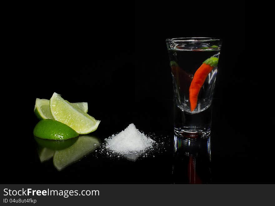 Shot glass filled with tequila with chili, lime and salt on a black background. Shot glass filled with tequila with chili, lime and salt on a black background