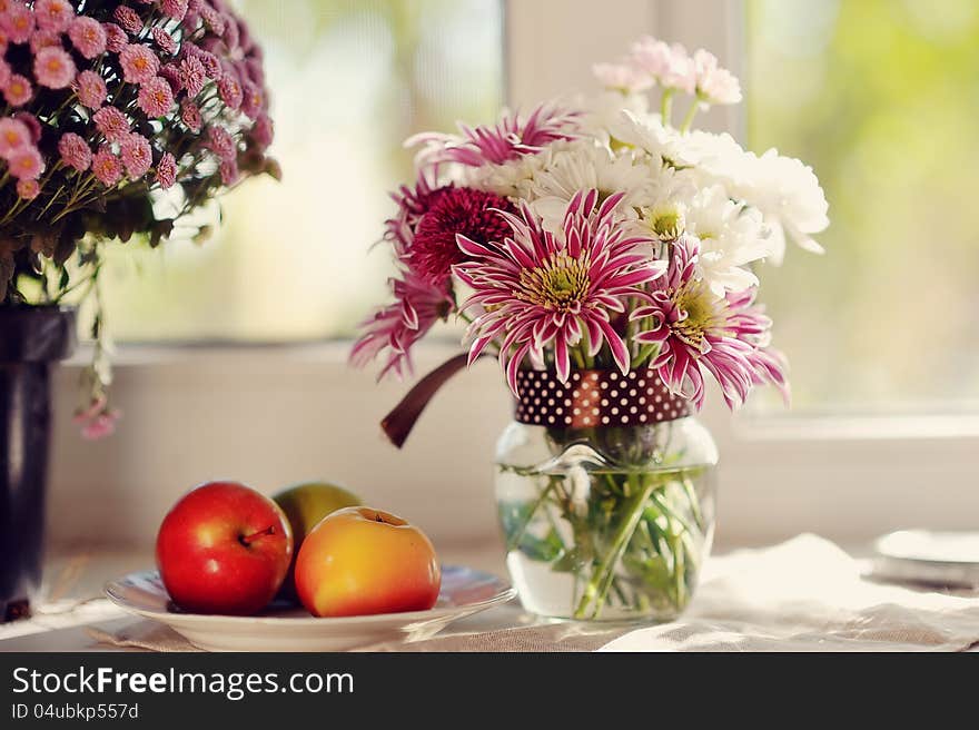 On a white plate ripe apples and bright bouquet of autumn flowers. On a white plate ripe apples and bright bouquet of autumn flowers