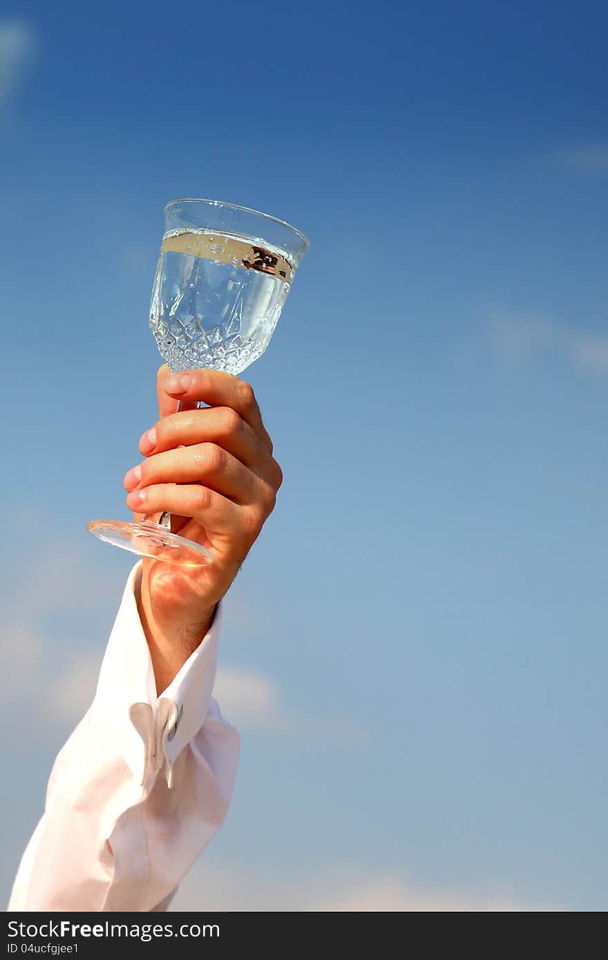 A glass of water held up in a toast against a bright cloudy blue sky background. A glass of water held up in a toast against a bright cloudy blue sky background