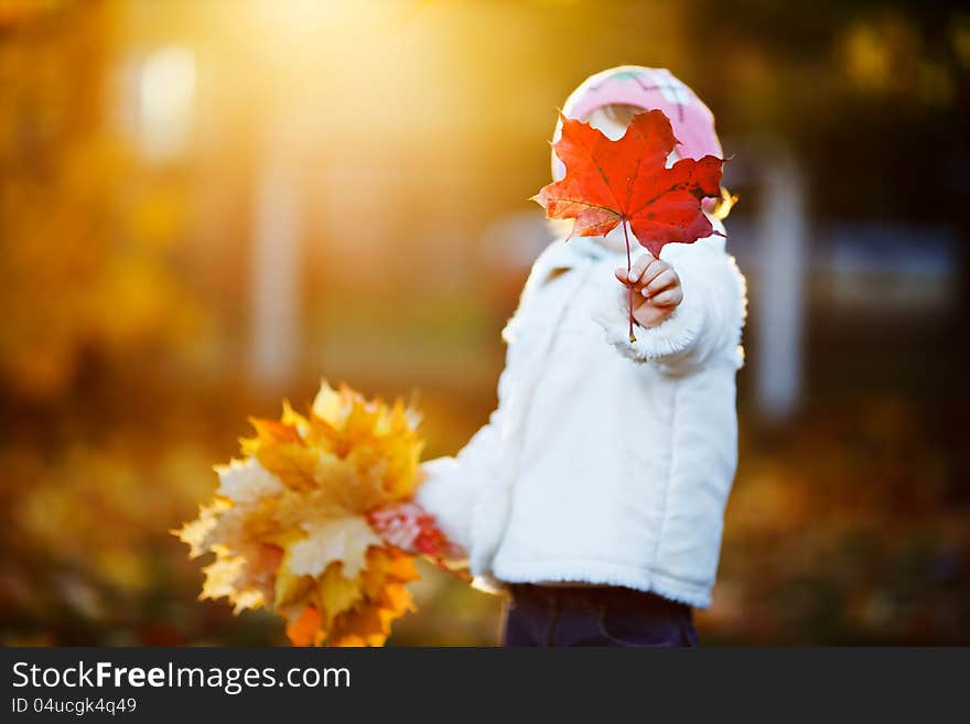 Small girl hiding her face with maple leaf