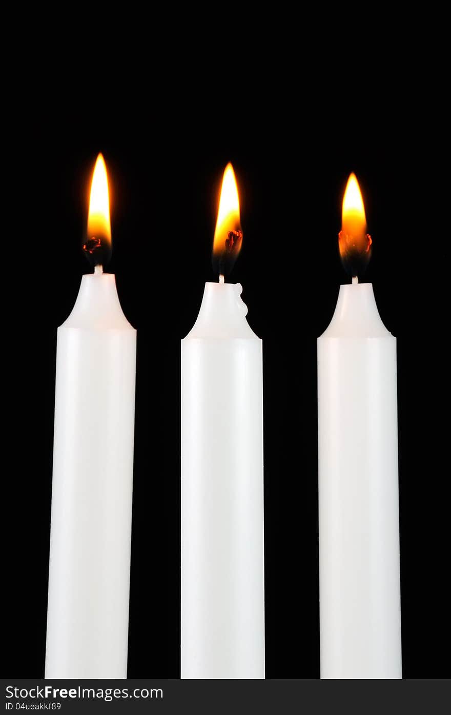 Three white burning candles in the dark against a black background