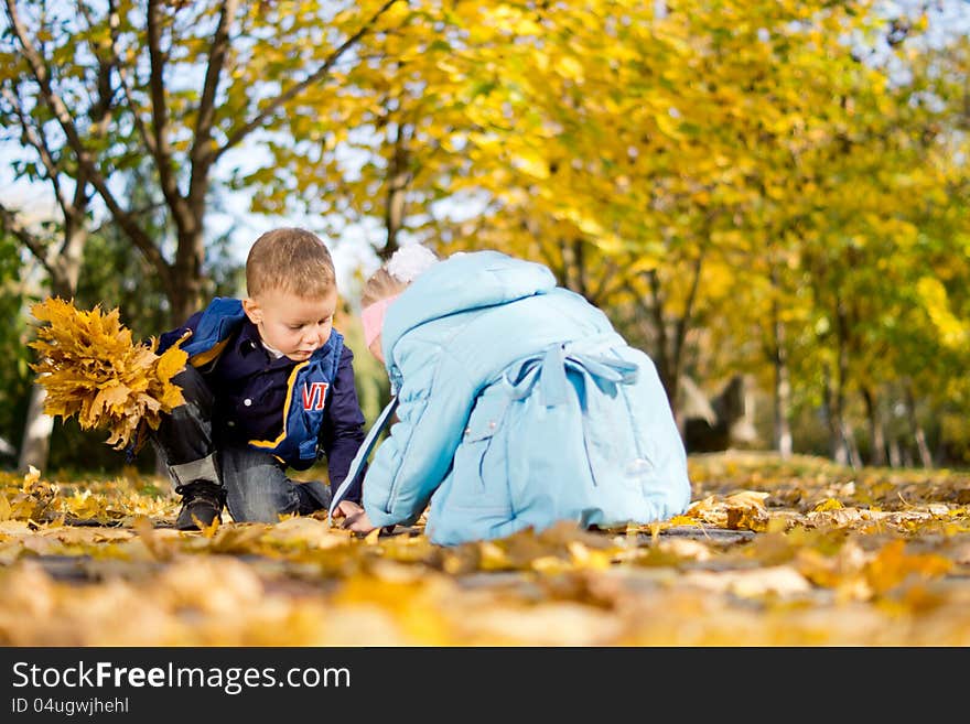 Low angle view of a young brother and sister kneeling on the ground in woodland playing in colourful yellow autumn or fall leaves. Low angle view of a young brother and sister kneeling on the ground in woodland playing in colourful yellow autumn or fall leaves