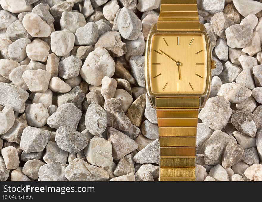 False gold wristwatch on a gravel background. False gold wristwatch on a gravel background