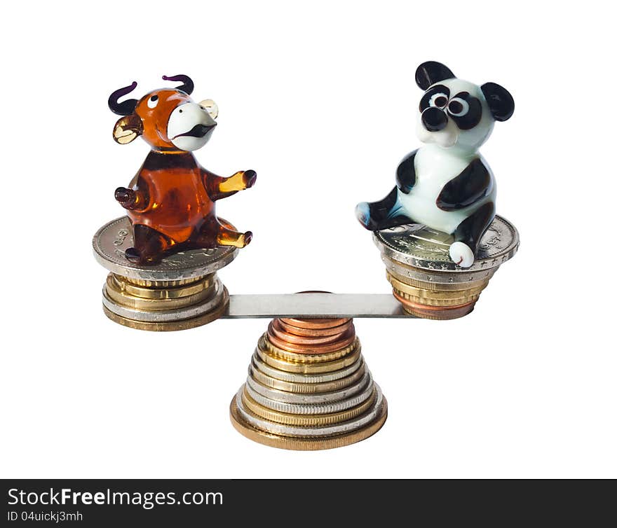 Bull and bear glass statuettes balancing with coins isolated on white background. Bull and bear glass statuettes balancing with coins isolated on white background