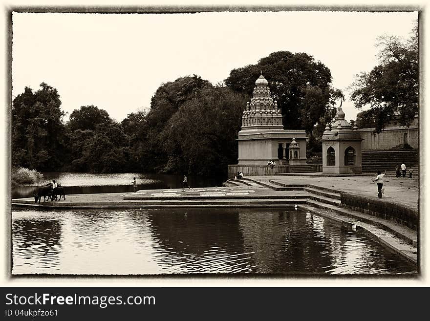 An Indian village scene showing a river side temple, people walking, kid flying kite and a man taking his cattle to drink water. An Indian village scene showing a river side temple, people walking, kid flying kite and a man taking his cattle to drink water