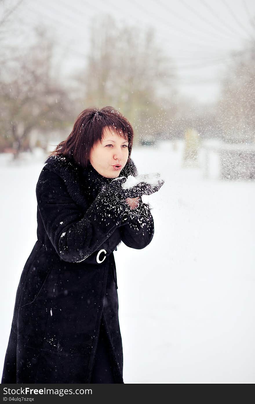 Outdoors in winter woman in a black fur coat playing with snow. Outdoors in winter woman in a black fur coat playing with snow