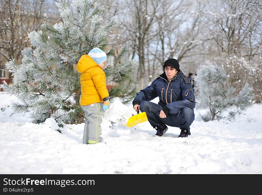 Winter child in a yellow jacket with a men playing in the snow. Winter child in a yellow jacket with a men playing in the snow