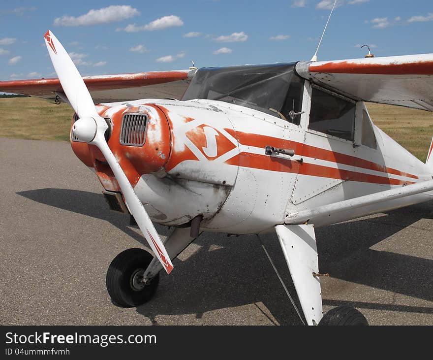 Close-up of the front of an old and weathered vintage tail-wheel, high-wing, single engine, red and white small private airplane on the ground. Close-up of the front of an old and weathered vintage tail-wheel, high-wing, single engine, red and white small private airplane on the ground.