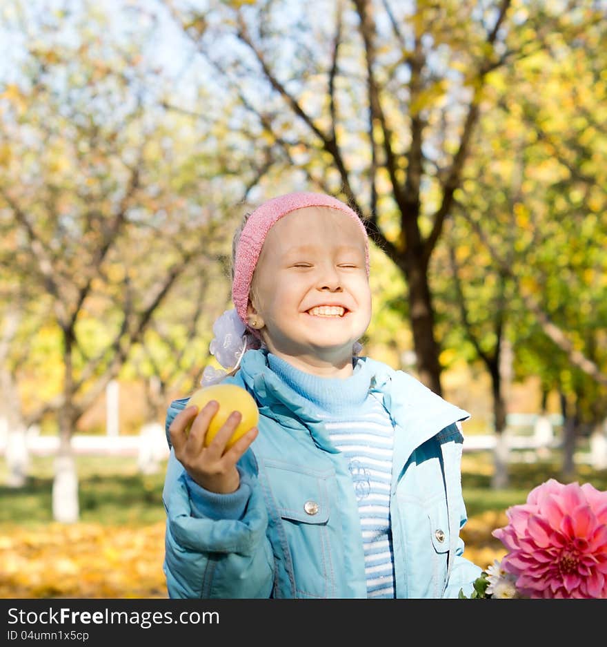 Little girl with a cheesy mischievous grin holding an apple and a fresh pink dahlia standing in colourful autumn countryside. Little girl with a cheesy mischievous grin holding an apple and a fresh pink dahlia standing in colourful autumn countryside