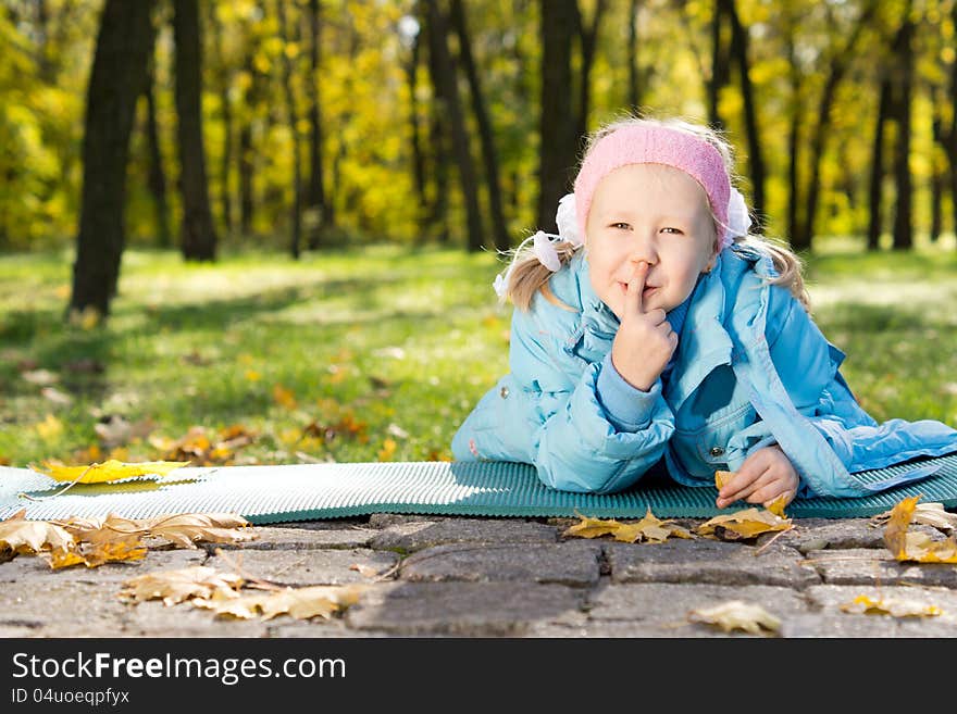 Smiling little girl lying on a mat in the park making shushing gesture raising her finger to her lips as a sign of silence or secrecy. Smiling little girl lying on a mat in the park making shushing gesture raising her finger to her lips as a sign of silence or secrecy