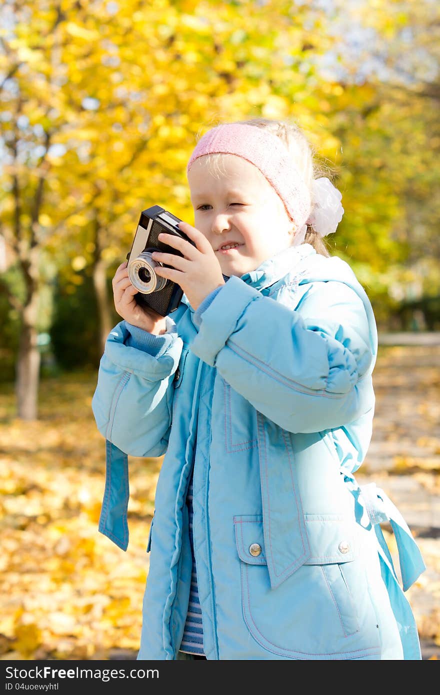 Aspiring young girl photographer trying to fathom out how to use a vintage slr camera as she stands outdoors in an autumn park