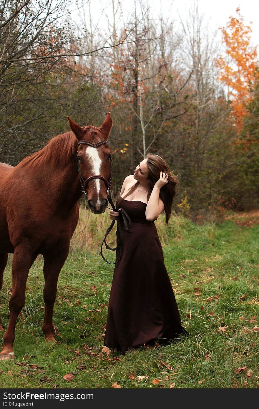 Pretty young woman in a long gown stands with her horse in Autumn. Pretty young woman in a long gown stands with her horse in Autumn.