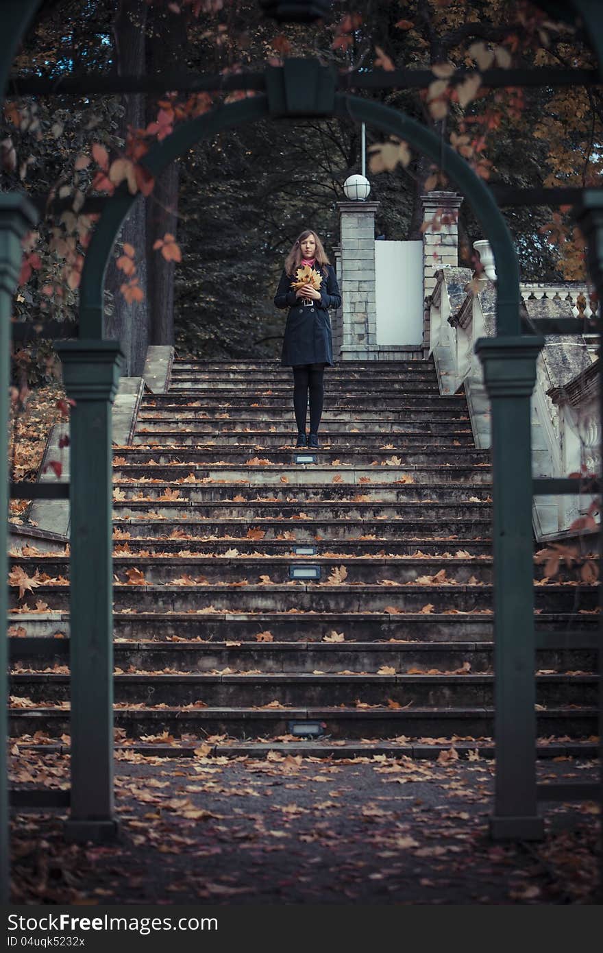 Girl stays on the stairs holding bunch of the leaves in her hands with arc on the foreground. Girl stays on the stairs holding bunch of the leaves in her hands with arc on the foreground