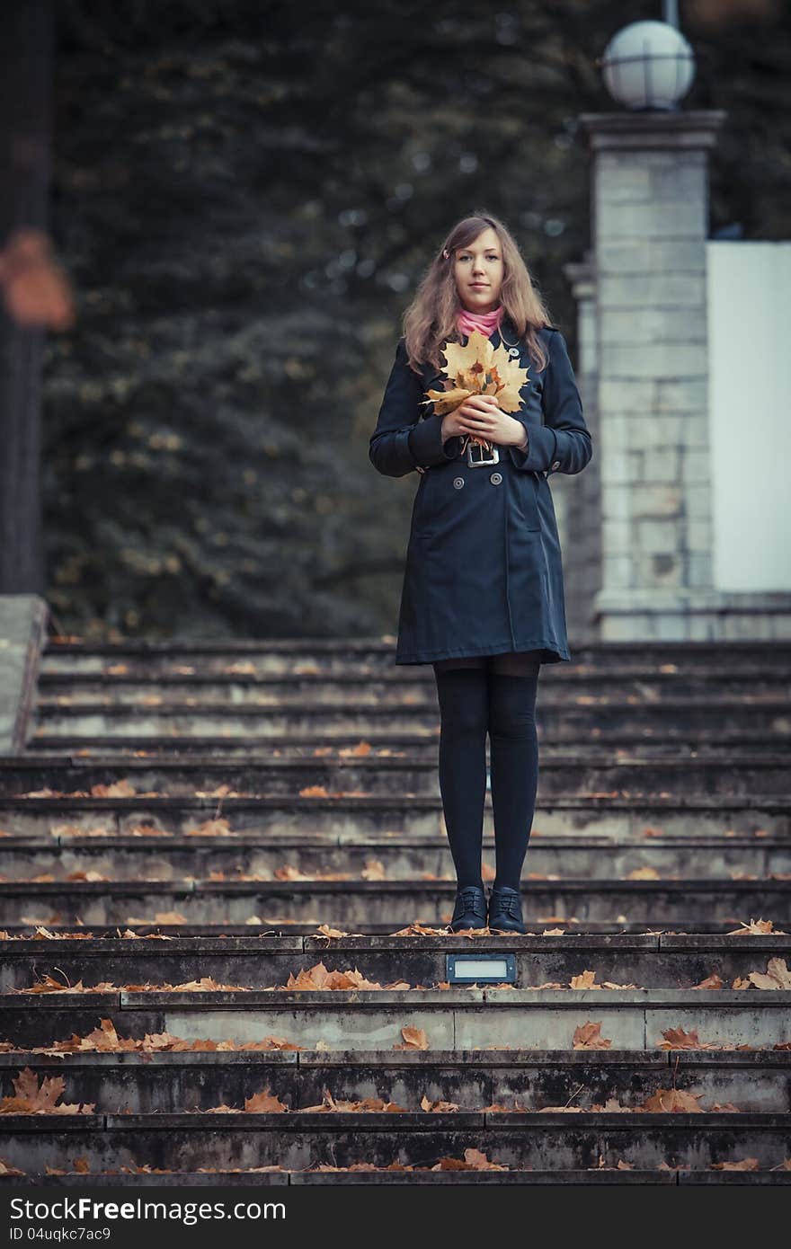 Girl stays on the stairs holding bunch of the leaves in her hands. Girl stays on the stairs holding bunch of the leaves in her hands