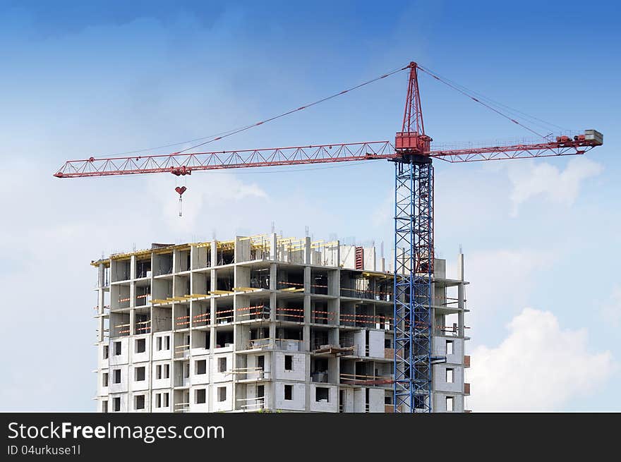 A tower crane and an unfinished building at a construction site against a blue sky background. A tower crane and an unfinished building at a construction site against a blue sky background