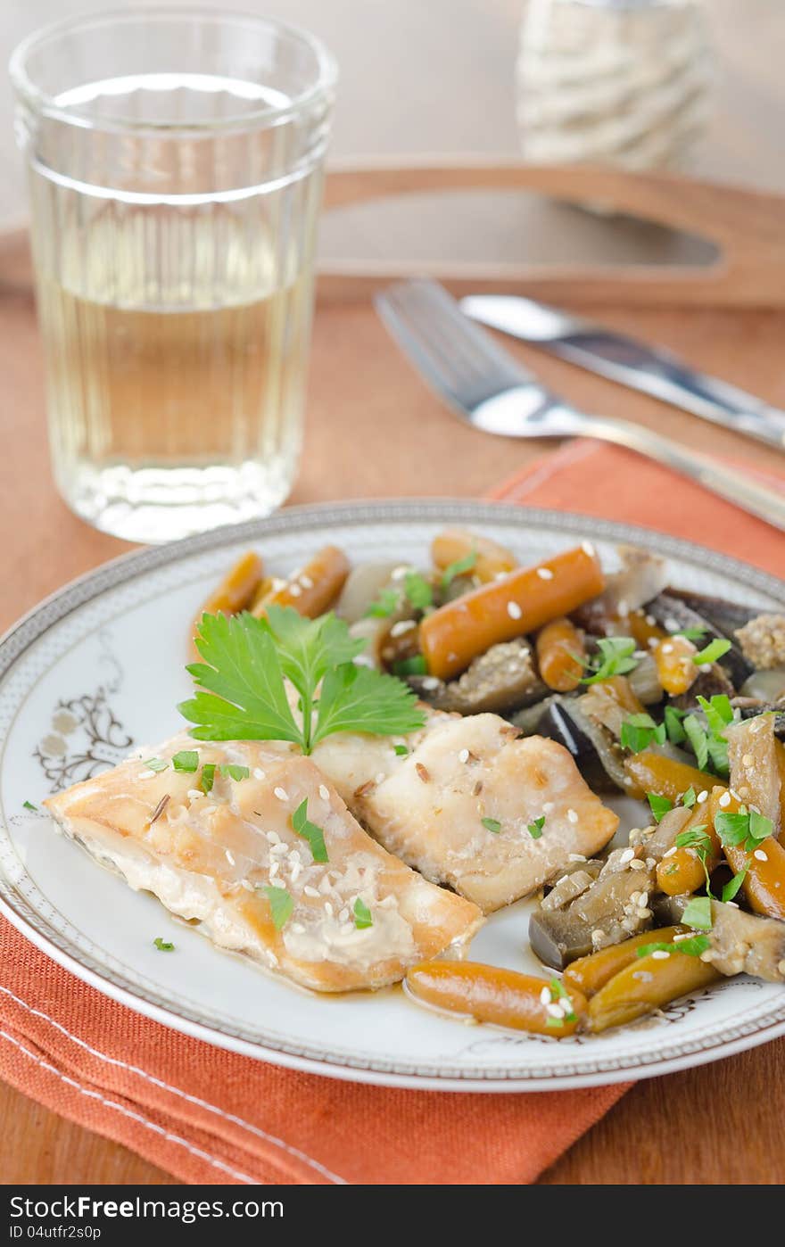 Sliced ​​baked cod with vegetables on the plate on the decorated table. Sliced ​​baked cod with vegetables on the plate on the decorated table