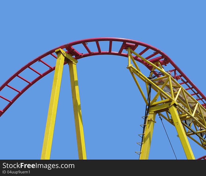 High curved section of red tracks for a roller coaster, with yellow support structures. against a blue sky. High curved section of red tracks for a roller coaster, with yellow support structures. against a blue sky.